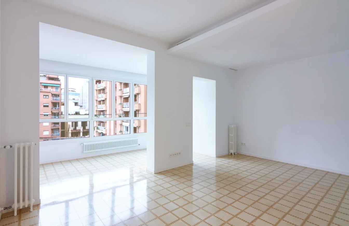 Imagen del salón de un piso totalmente reformado con un gran ventanal, paredes blancas y suelo enlosado