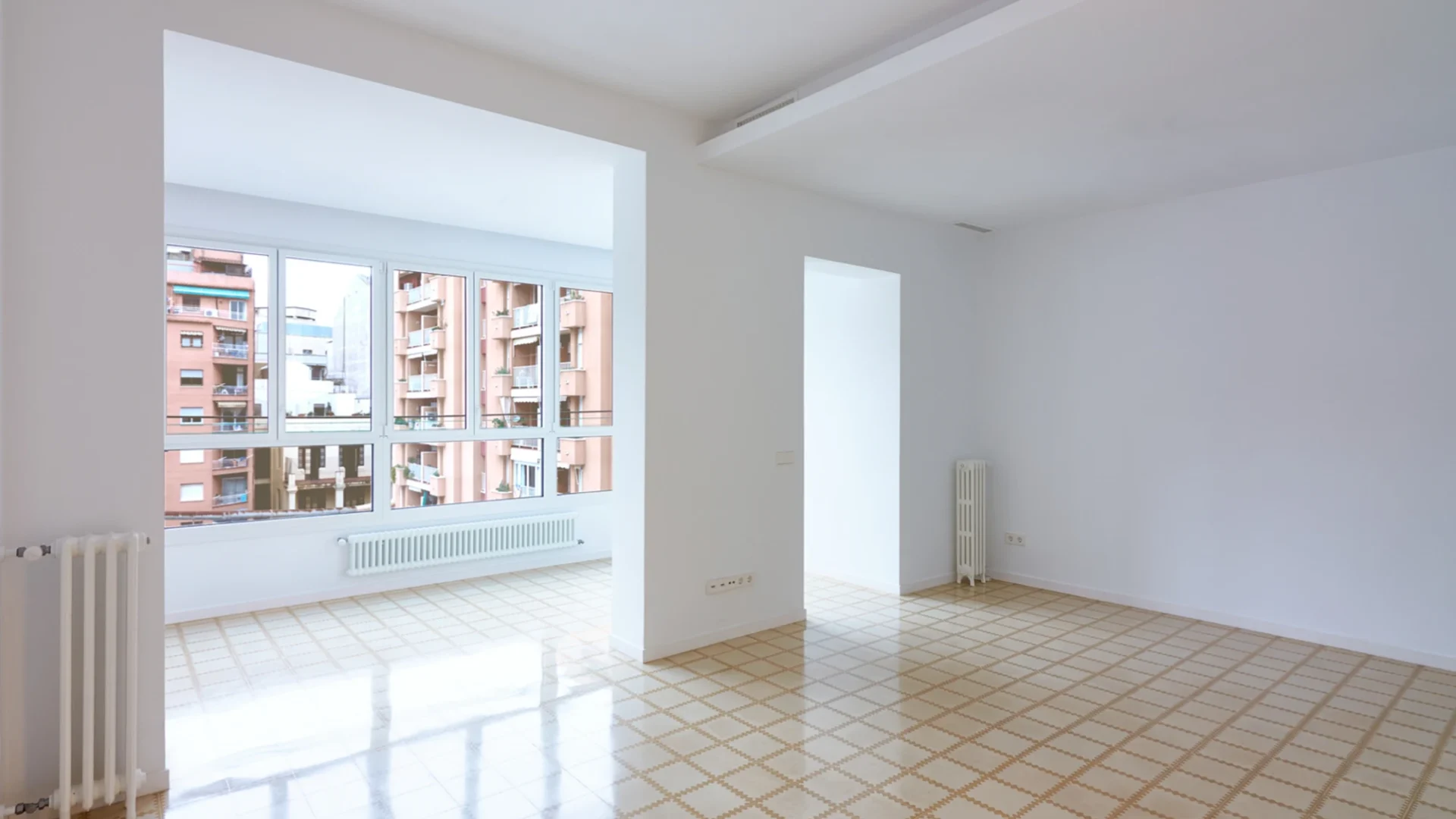 Imagen del salón de un piso totalmente reformado con un gran ventanal, paredes blancas y suelo enlosado