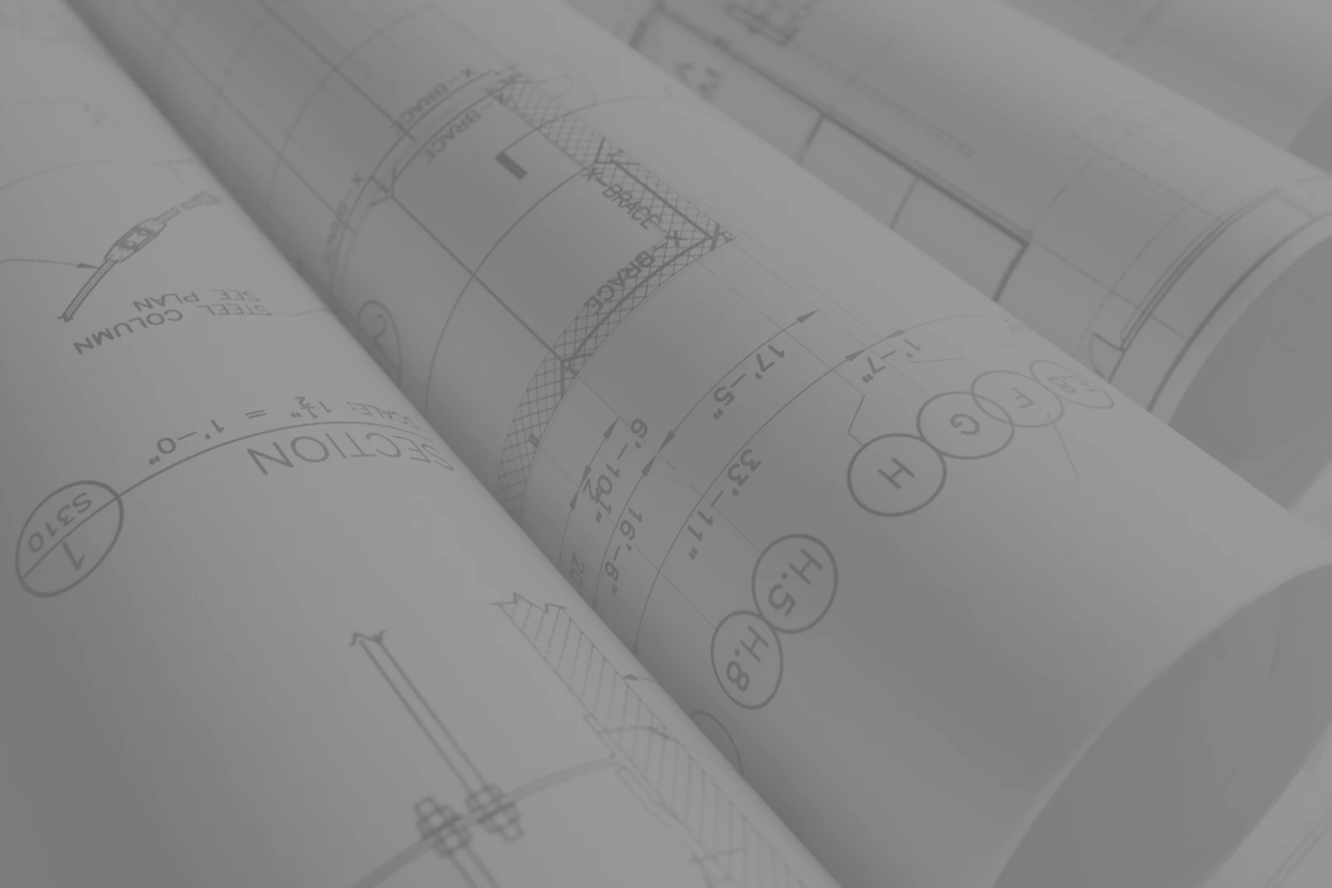 Imagen de varios planos de arquitectura enrollados que muestran dibujos técnicos de delineación