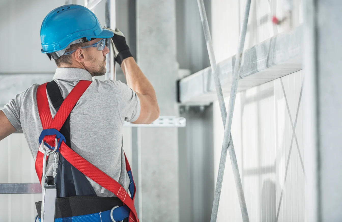 Trabajador de la construcción subido a un andamio debidamente equipado con su casco, gafas de protección y arnés de seguridad