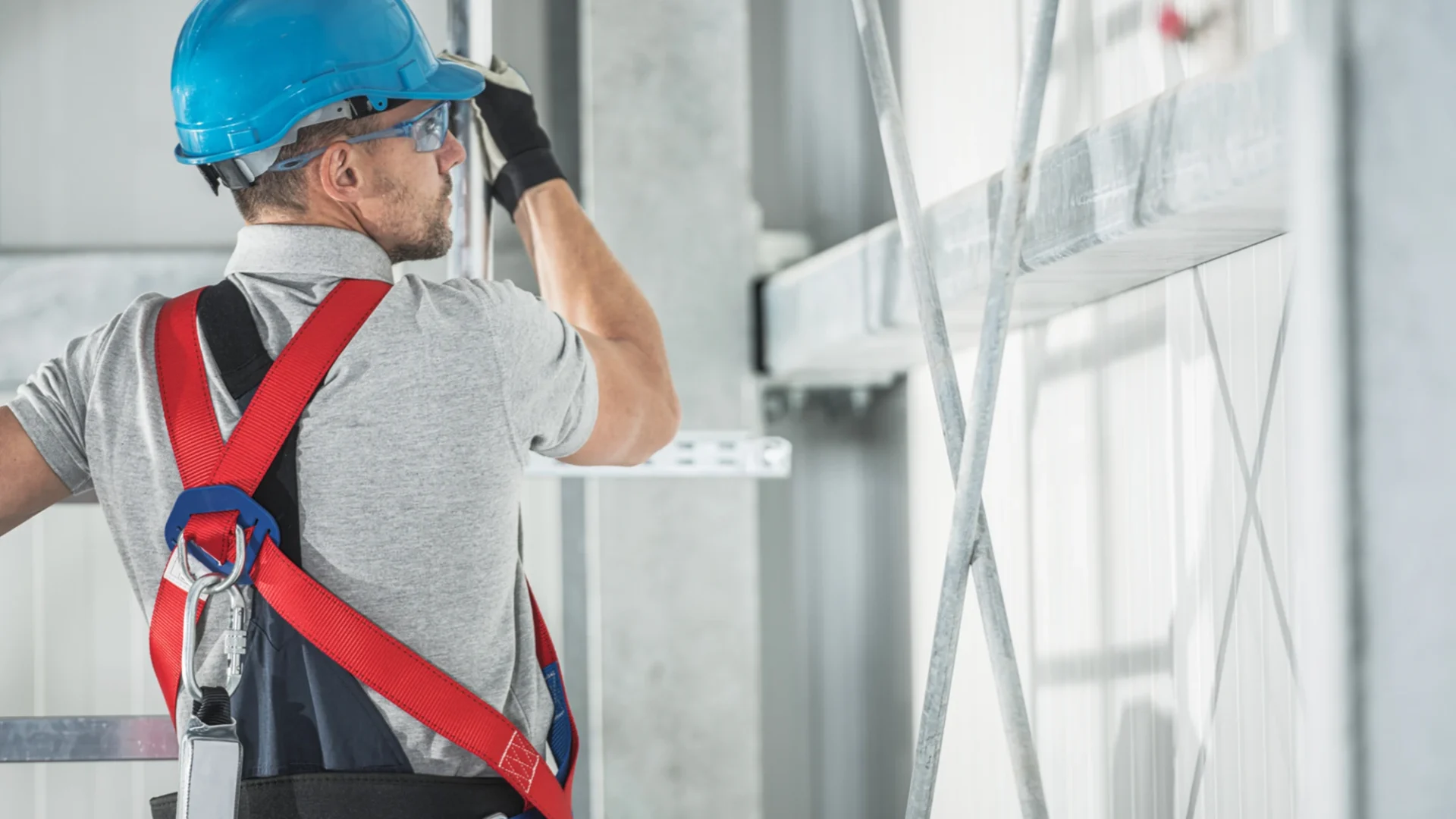 Trabajador de la construcción subido a un andamio debidamente equipado con su casco, gafas de protección y arnés de seguridad